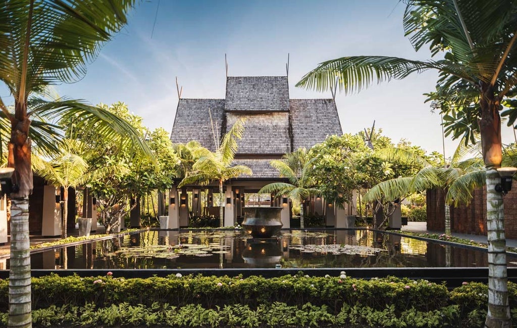 Modern beachfront resort with infinity pool stretching towards white sand beach, surrounded by lush tropical gardens and palm trees