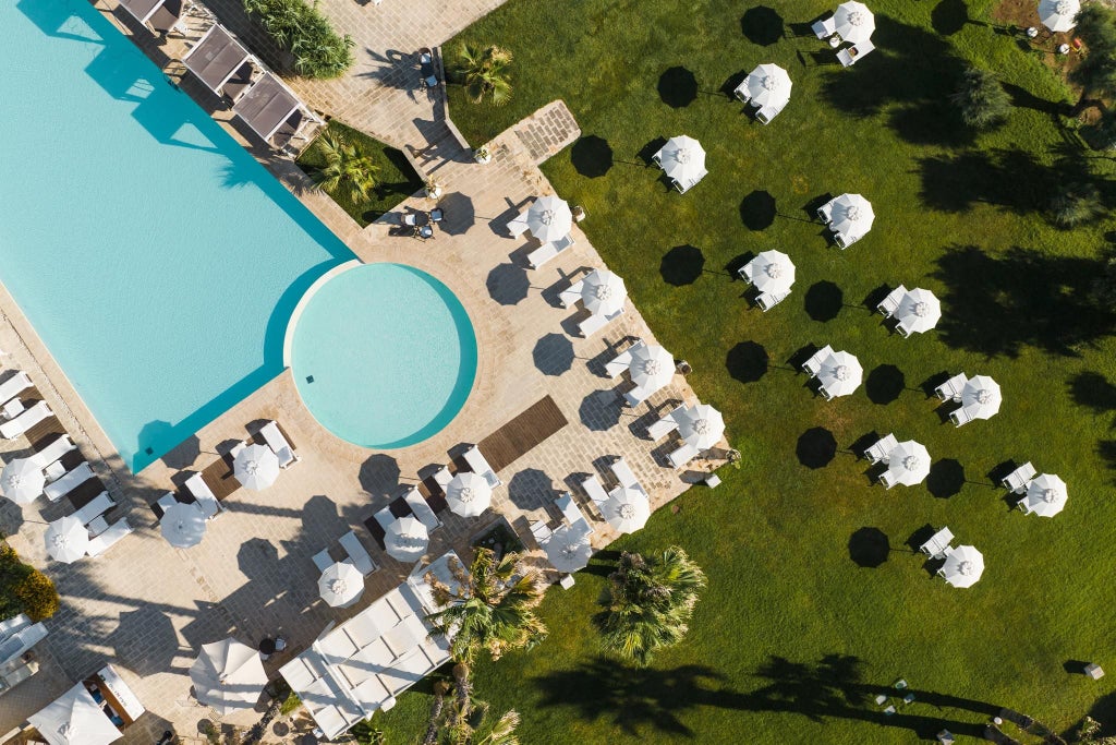 Luxurious white-washed coastal hotel with minimalist design, set against azure Mediterranean backdrop, featuring elegant pool and sun loungers in Torre Canne, Italy