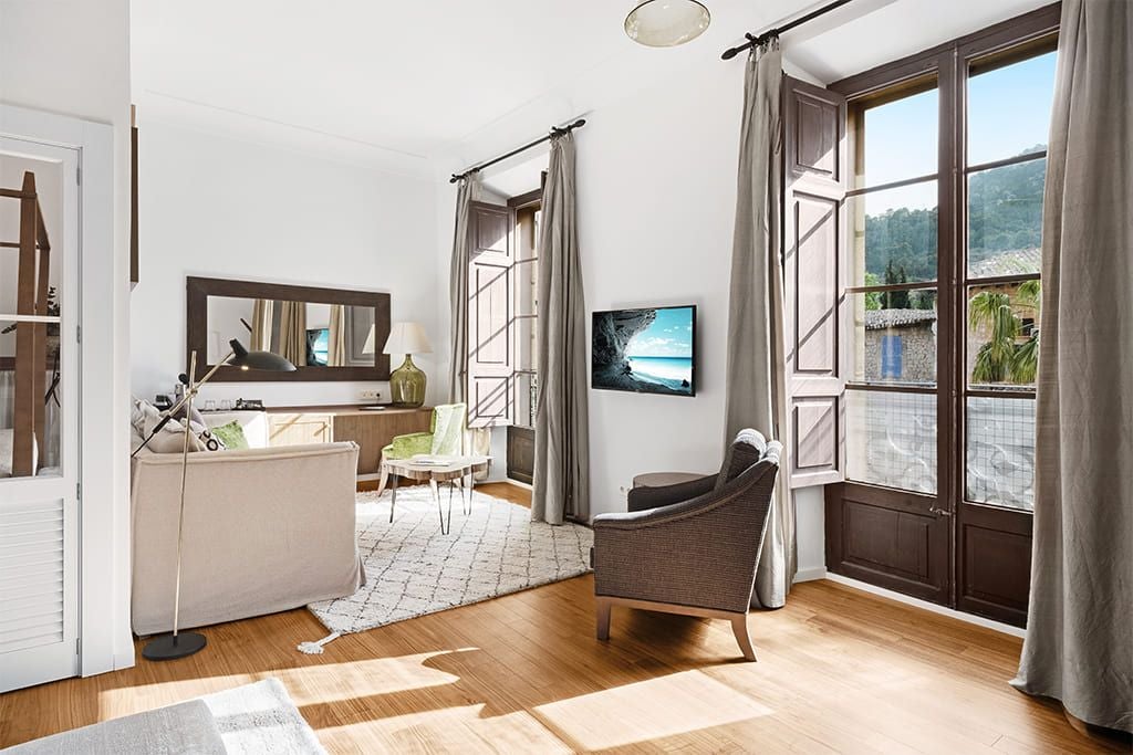 Luxurious junior suite at scenset hotel in Sóller, Spain, featuring elegant white decor, modern furnishings, and a spacious balcony with mountain views