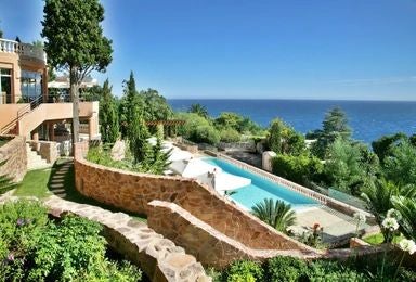 Luxurious coastal hotel with Mediterranean blue waters, white facade, and elegant terrace overlooking scenic French Riviera landscape near Cannes