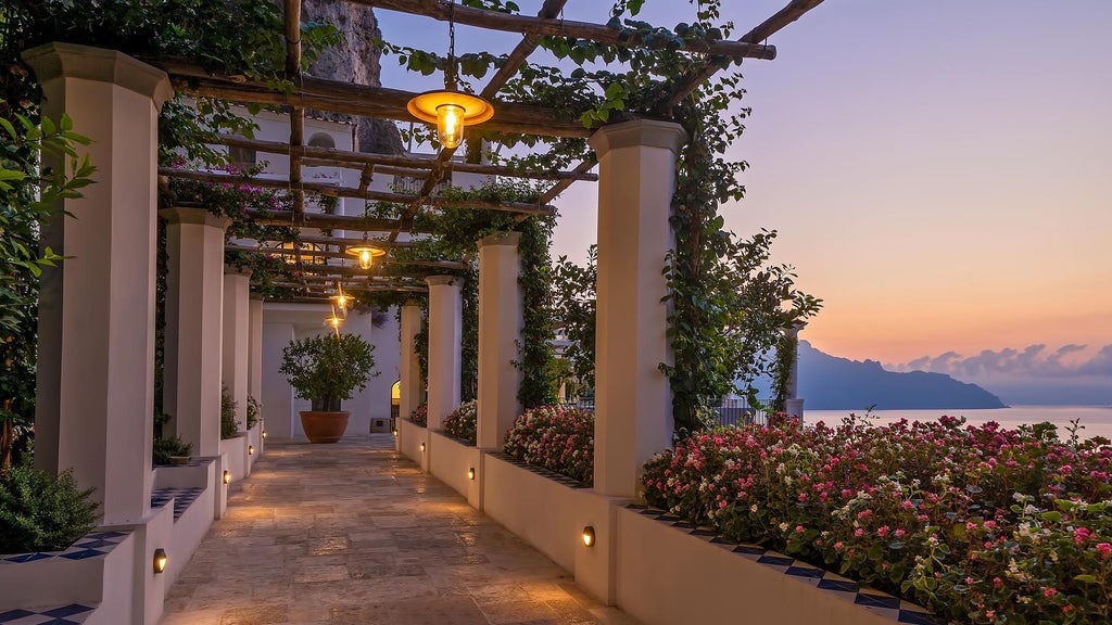 Elegant cliffside hotel in Amalfi Coast, featuring white terraces and infinity pool overlooking Mediterranean's azure waters at sunset