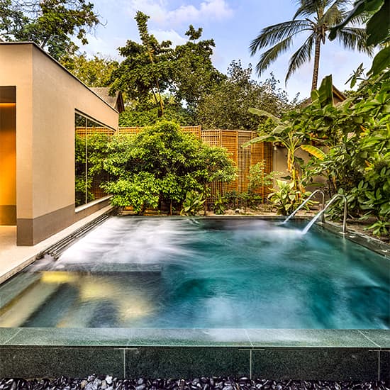 Luxury Maldivian water villa with private infinity pool extends over turquoise lagoon, surrounded by tropical palms at sunset