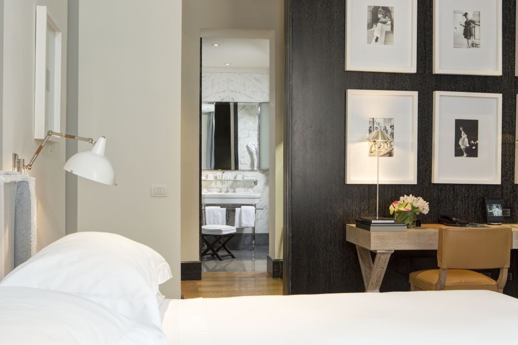 Elegant marble-adorned hotel room with plush king bed, floor-to-ceiling windows overlooking Roman streetscape, luxurious contemporary Italian design