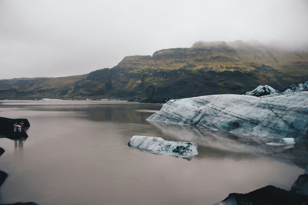 All-terrain vehicle traversing black volcanic sand near a weathered plane wreck with rugged Icelandic landscape in the background, showcasing an adventurous off-road expedition across dramatic terrain.