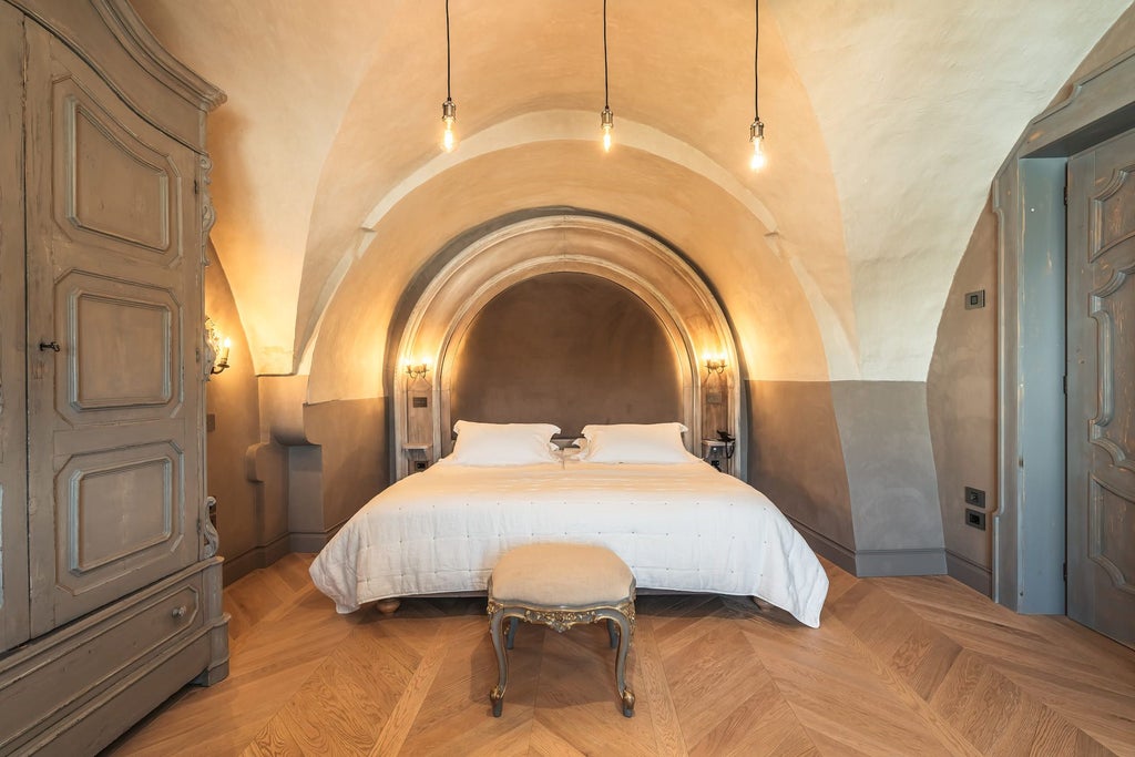 Elegant Deluxe Room at Scenic Italian Boutique Hotel with plush king bed, soft neutral tones, and large arched window overlooking historic landscape