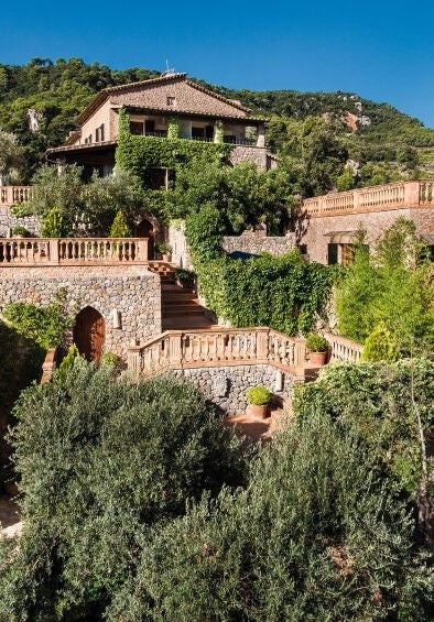 Elegant Mediterranean hotel nestled in Mallorca's mountains with stone facade, traditional shutters and lush garden terraces