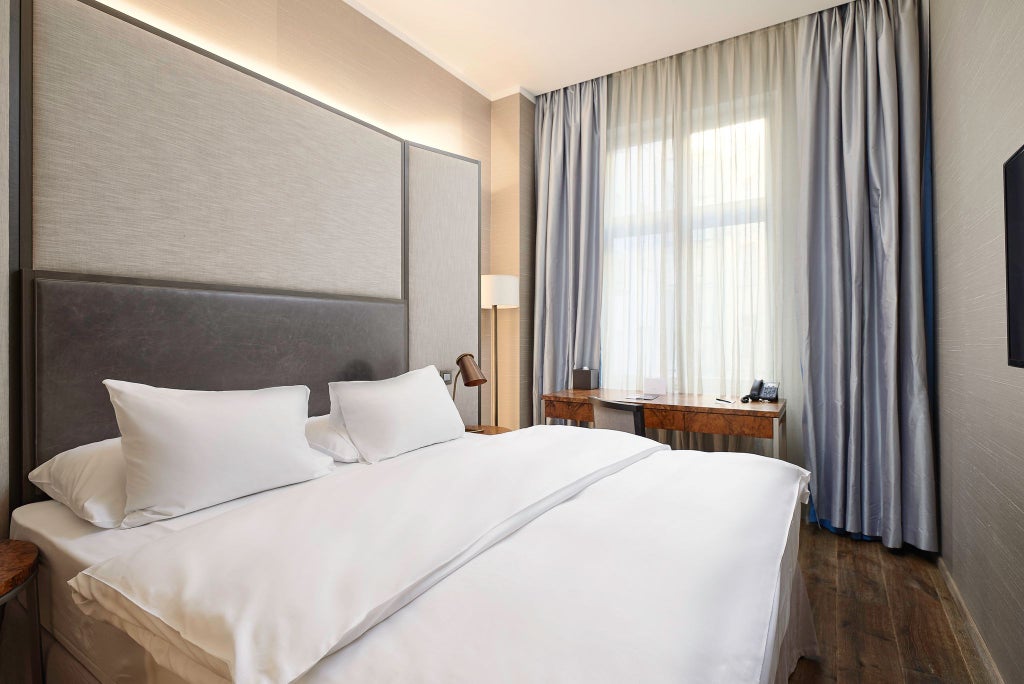 Elegant petite hotel room with sophisticated gray decor, plush white bedding, modern minimalist design, large window overlooking urban scenery in Prague