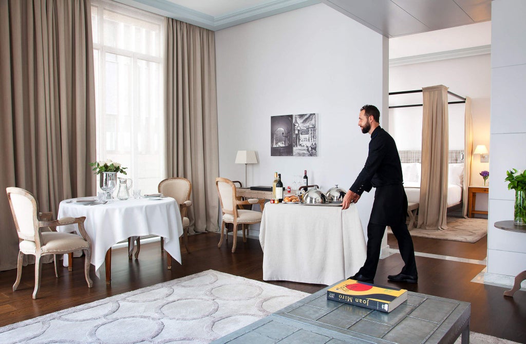 Elegant URSO Suite with plush king bed, rich wood furnishings, soft neutral color palette, and sophisticated Spanish design details in Madrid luxury hotel room