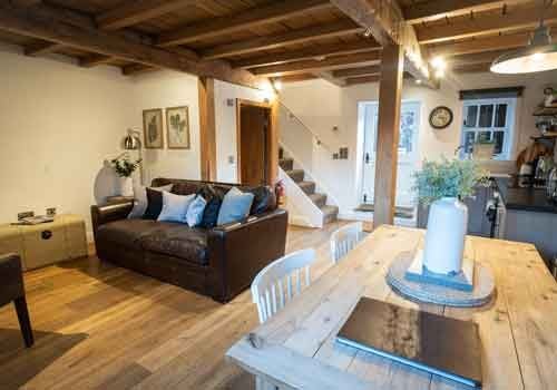 Elegant barn-style luxury suite with modern furnishings, featuring plush king bed, exposed wooden beams, and soft neutral color palette in UK countryside setting