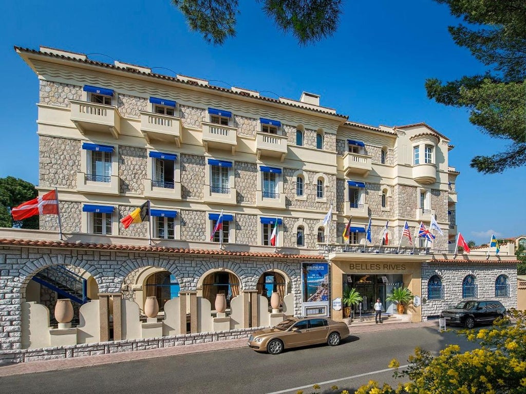 Art Deco waterfront hotel with elegant white facade, private beach pier, and Mediterranean views from multiple terraces in French Riviera setting