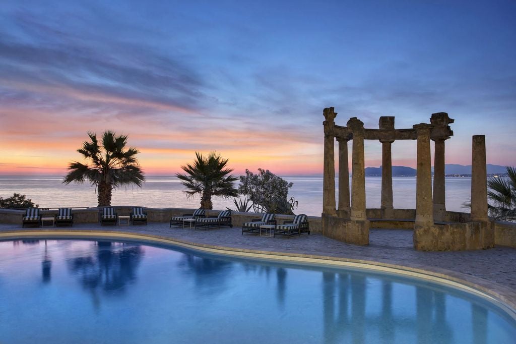 Grand waterfront Villa Igiea hotel in Sicily with manicured gardens, ornate Renaissance architecture, and palm trees against blue sky