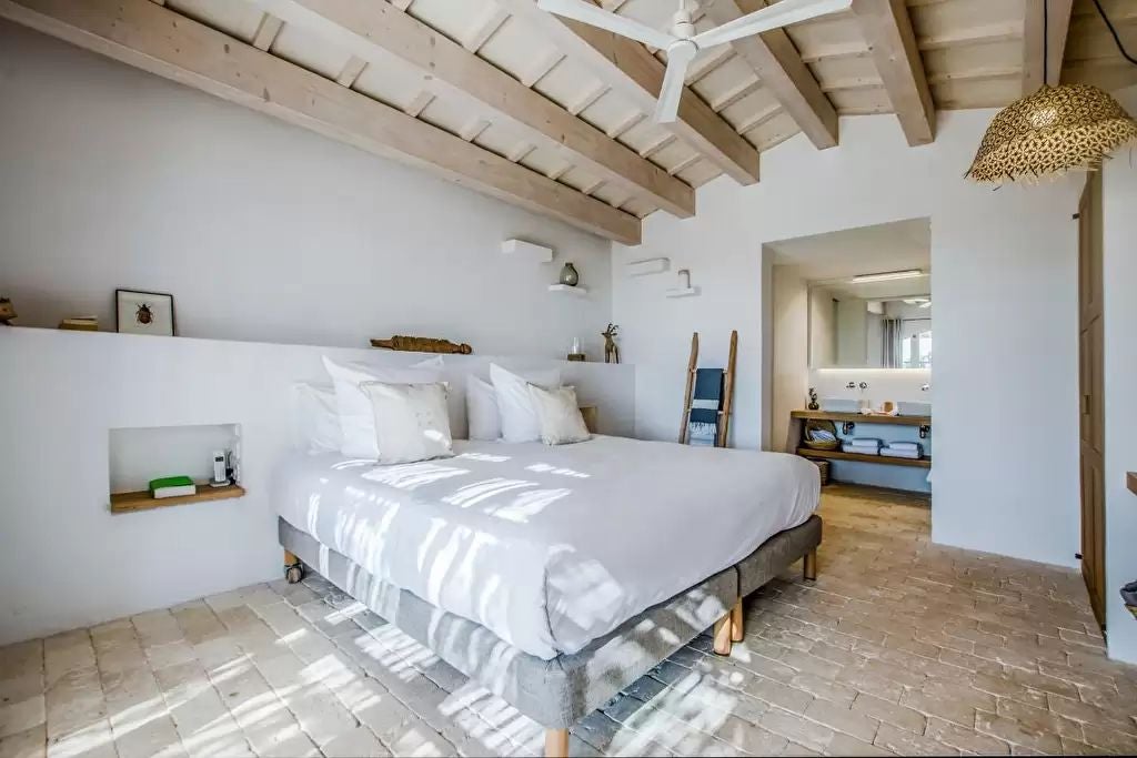 Elegant classic hotel room with warm wood furnishings, plush white bedding, and large window overlooking scenic Mediterranean landscape in Spain