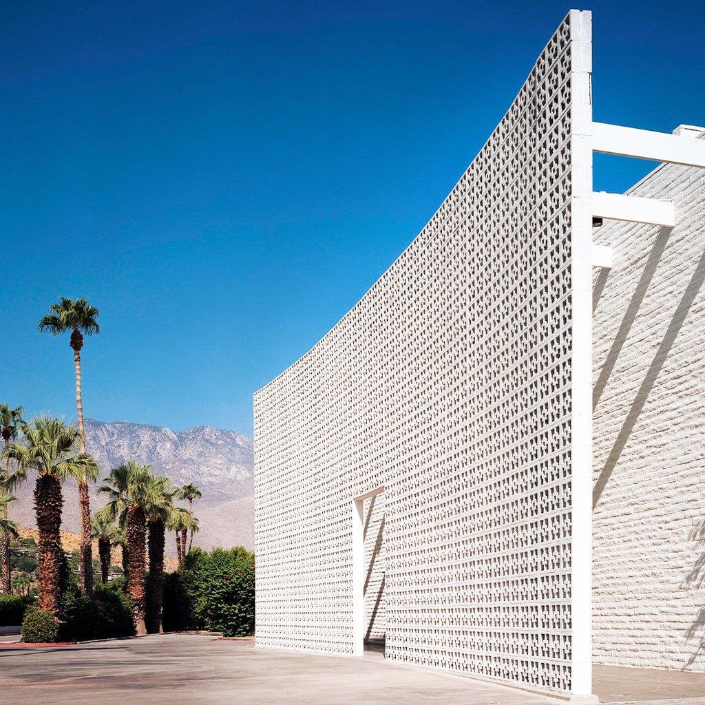 Elegant white Spanish colonial-style hotel exterior with towering palm trees, manicured gardens and luxurious poolside terrace in Palm Springs