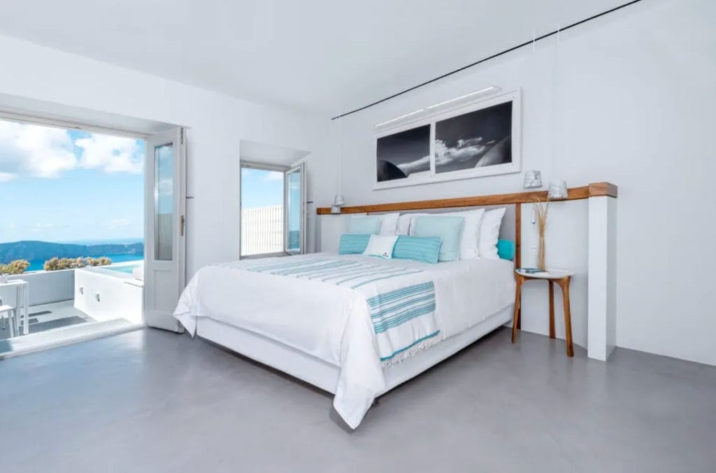 Modern white-walled hotel room with private plunge pool, ocean views, minimalist decor and loungers on a stone terrace in Santorini