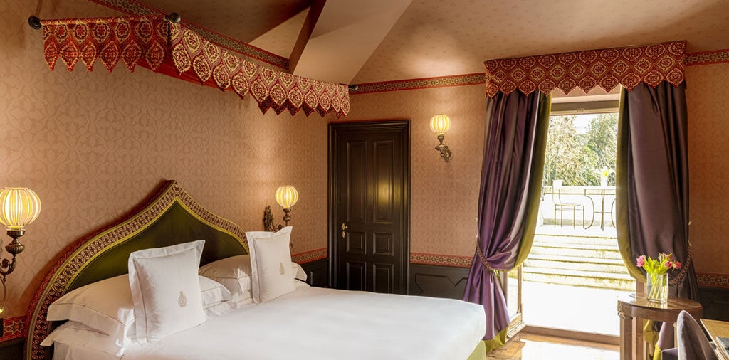 Elegant hotel room with crystal chandelier, antique gilded furniture, ornate walls, and floor-to-ceiling windows overlooking Italian garden