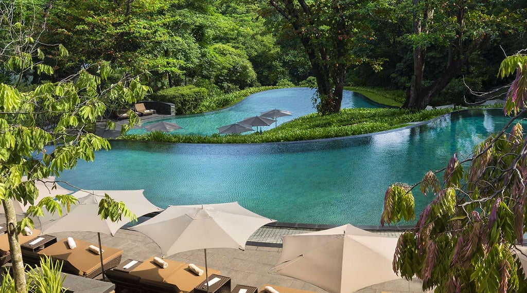 Elegant colonial-style luxury hotel with curved white facade, surrounded by lush tropical gardens and palm trees at sunset in Singapore