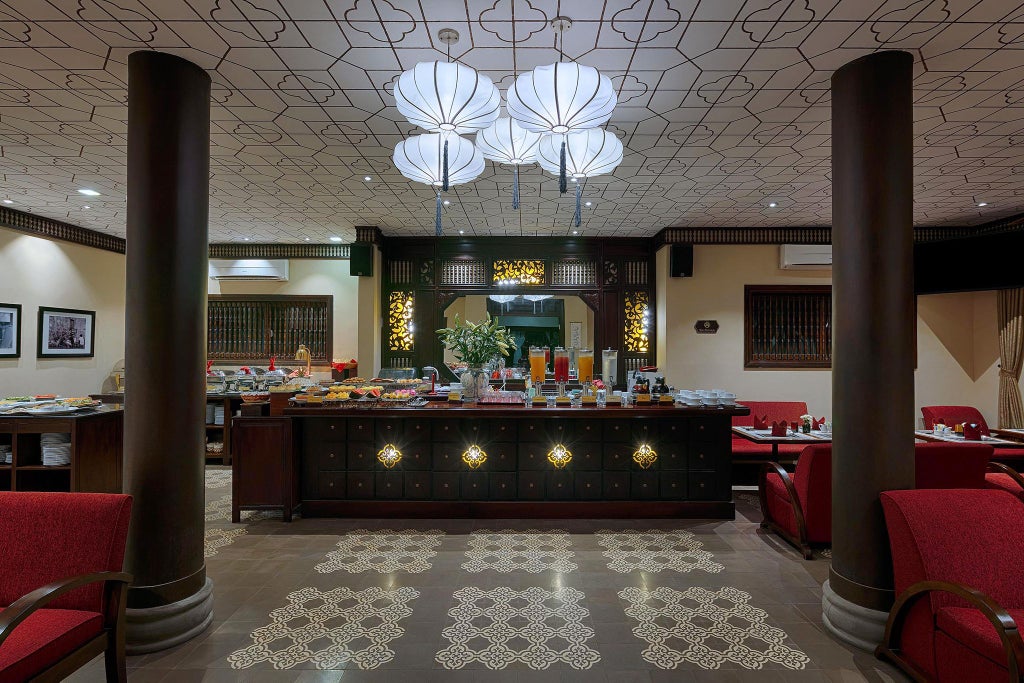 Elegant boutique hotel facade with traditional Vietnamese architectural style, lush tropical greenery, and warm golden lighting at dusk in Hoi An