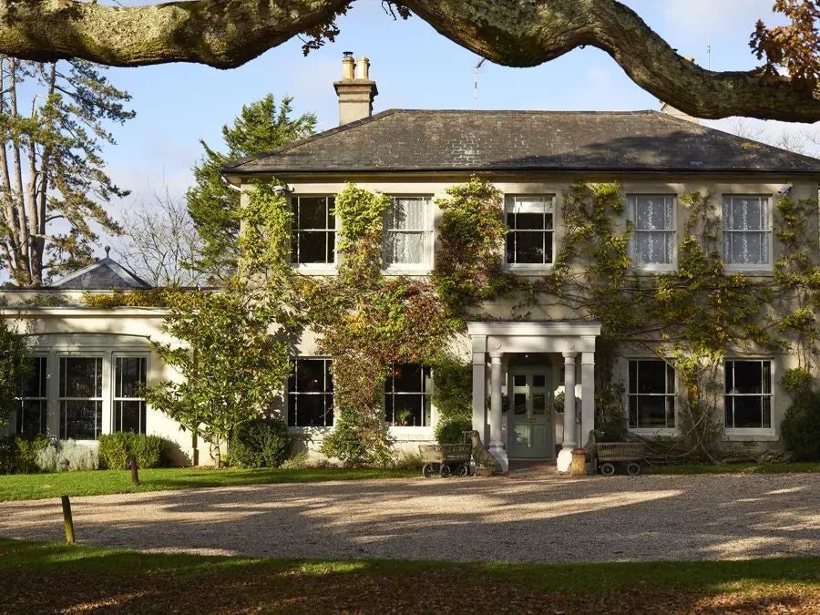 Coastal luxury hotel with rustic-chic design, nestled against sandy beach with weathered wooden deck and lush seaside vegetation, UK coastal charm