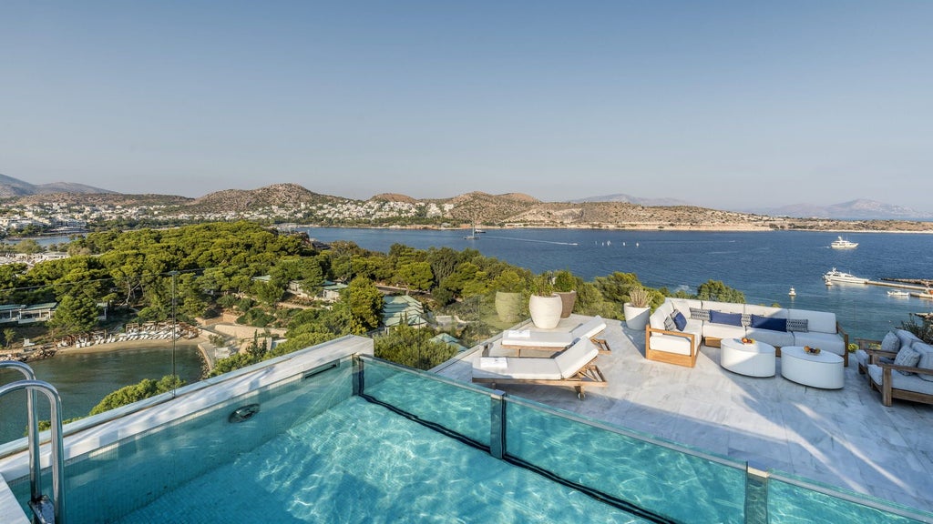 Elegant hotel suite with floor-to-ceiling windows framing sea views, modern furnishings, and a private balcony overlooking the Aegean Sea