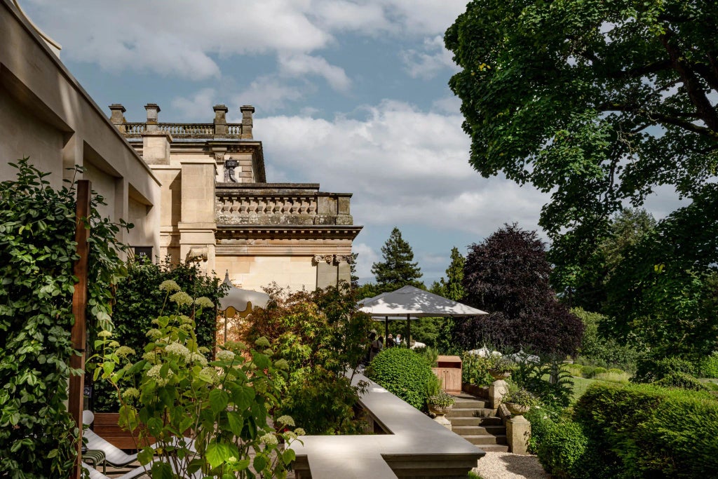 Luxurious countryside hotel exterior with contemporary architecture, stone facade, and manicured gardens nestled in the scenic Cotswolds landscape.