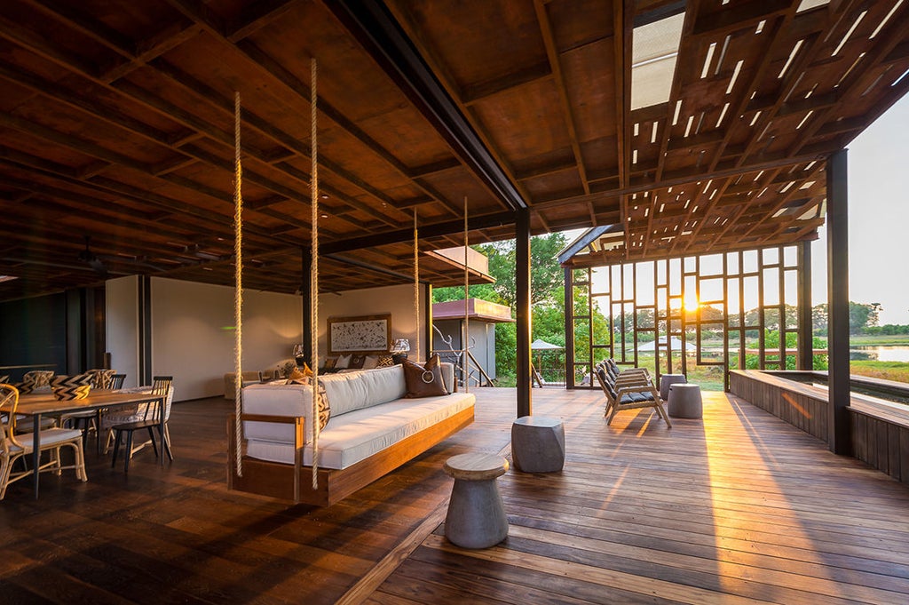 Modern timber-framed luxury lodge with glass walls overlooking serene wetlands, featuring a raised deck and natural color palette