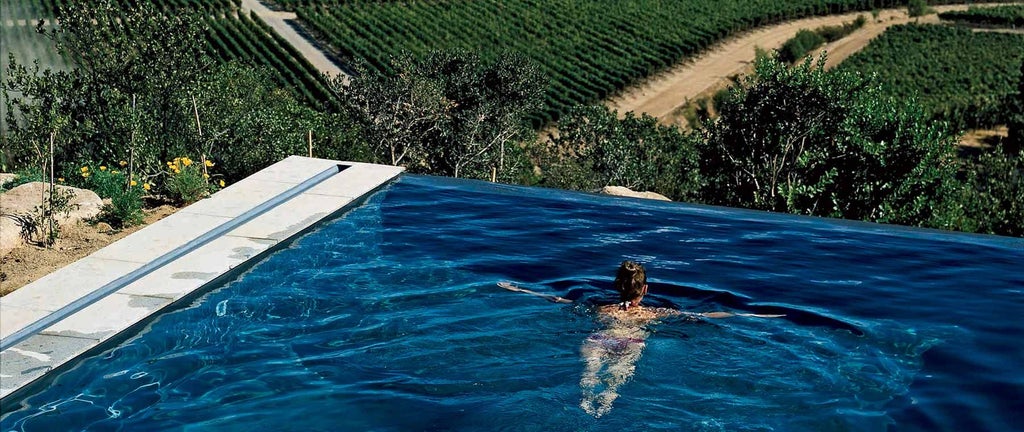 Luxury wine estate nestled in Chile's lush landscape, with modern architecture blending seamlessly into rolling vineyard hills and distant mountains.