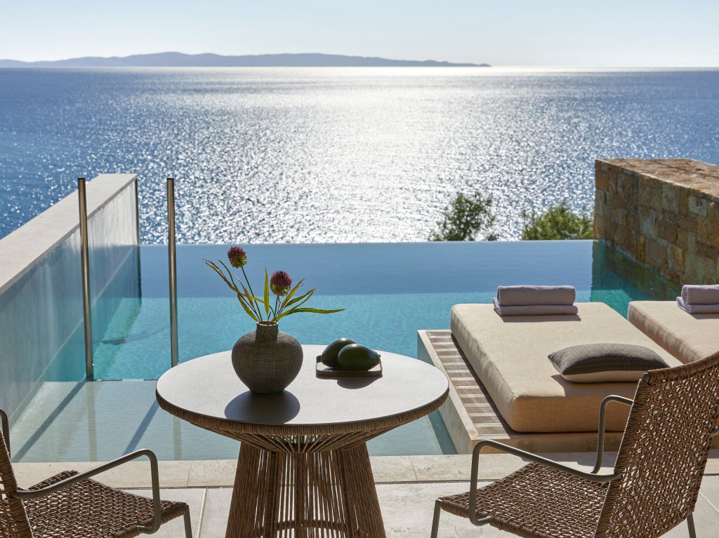 Luxurious infinity pool overlooking azure Ionian Sea, with elegant white sun loungers and sleek Mediterranean resort architecture at Scenset hotel in Greece