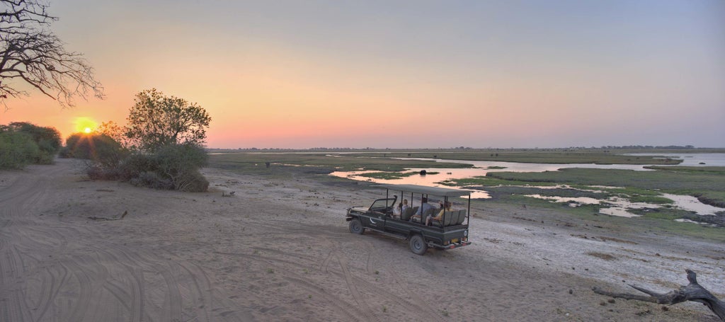 Luxurious safari tent camp overlooking Chobe River with canvas lodgings nestled among acacia trees at sunset in Botswana wilderness