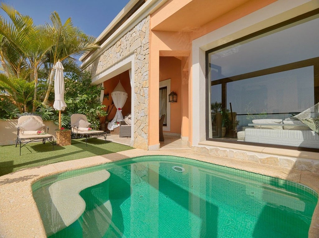 Elegant stone villa with arched windows and terracotta roof amid lush garden, featuring private pool and mountain views in Spain