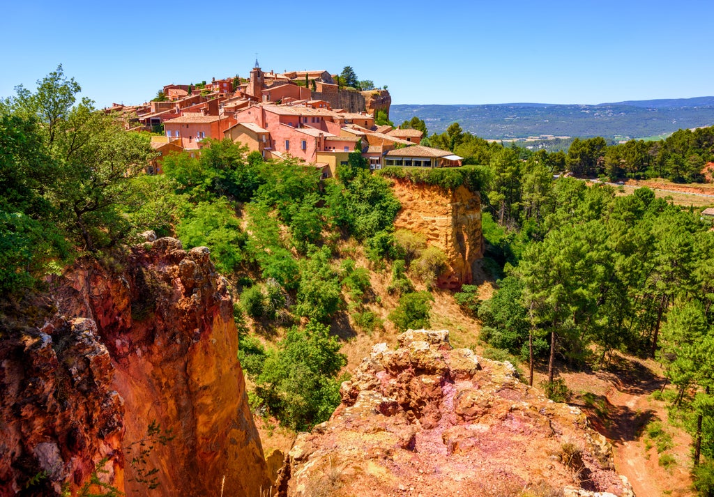 Sunlit stone houses nestled in Luberon Valley village, with blooming lavender fields and cypress trees against Provence hills