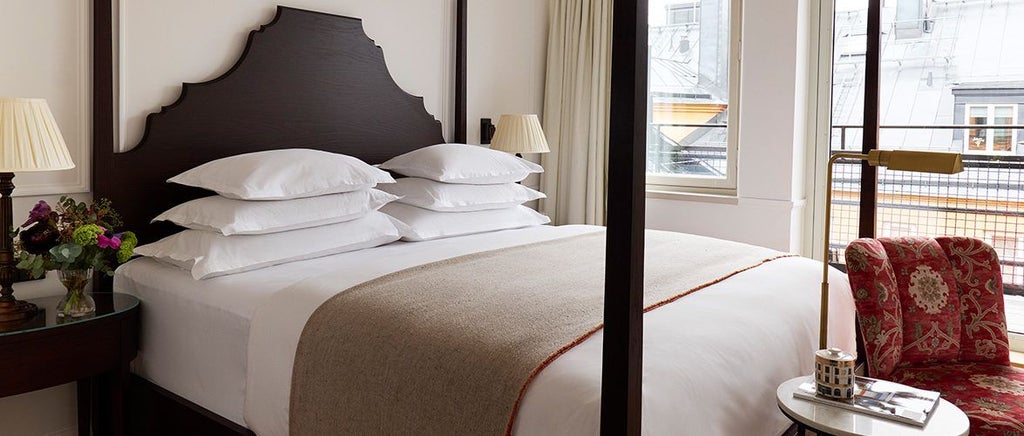 Elegant Scandinavian-style deluxe hotel room with wooden floors, plush white bedding, contemporary furnishings, and large glass doors opening to private balcony