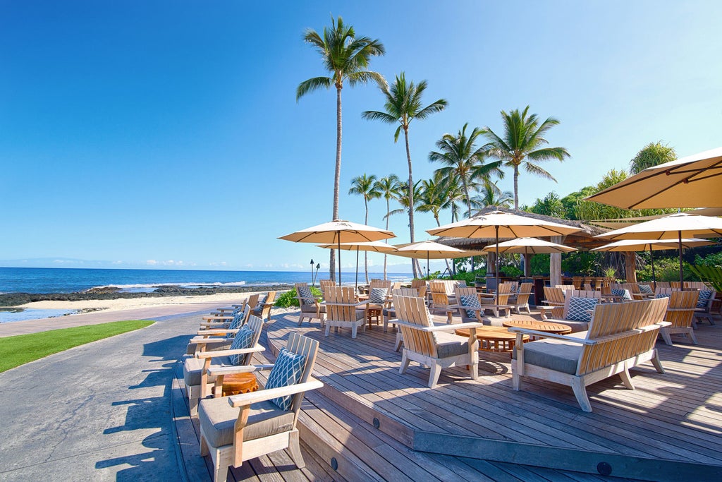 Luxury oceanfront resort with infinity pool overlooking Pacific Ocean, palm trees and volcanic rock landscape at sunset in Hawaii