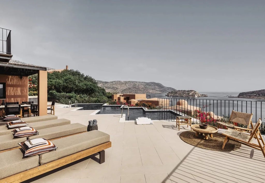 Luxurious beachfront resort with white-domed suites overlooking azure Aegean waters, set against dramatic Cretan landscape and pristine coastline.