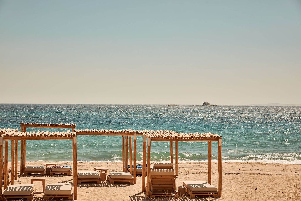 Luxurious beachfront hotel with white-washed walls, blue accents, infinity pool overlooking crystal-clear Aegean waters, Cycladic architecture in Naxos, Greece