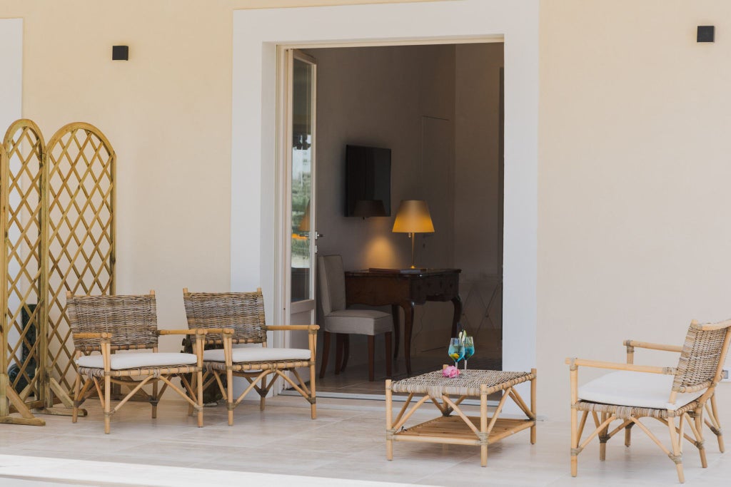 Elegant Sicilian boutique hotel room with soft neutral tones, antique furniture, plush white linens, and traditional architectural details in a restored villa