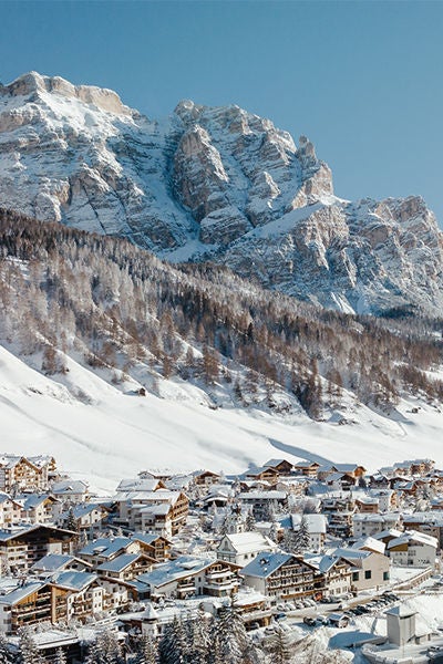 Elegant stone and timber alpine hotel nestled in Italian Dolomites, featuring wooden balconies and snow-capped mountain backdrop at sunset