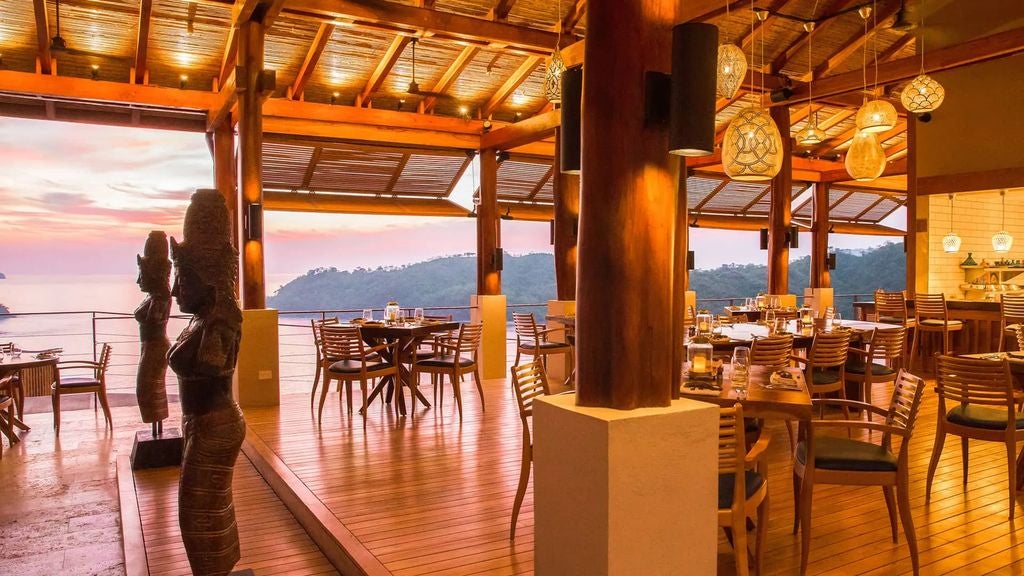 Infinity pool overlooking lush Costa Rican jungle and Pacific Ocean at sunset, with modern lounge chairs and tropical villa views