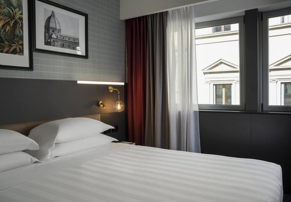 Elegant modern double room with crisp white linens, sleek minimalist design, large window, warm wood accents, and contemporary Italian hotel styling in Florence