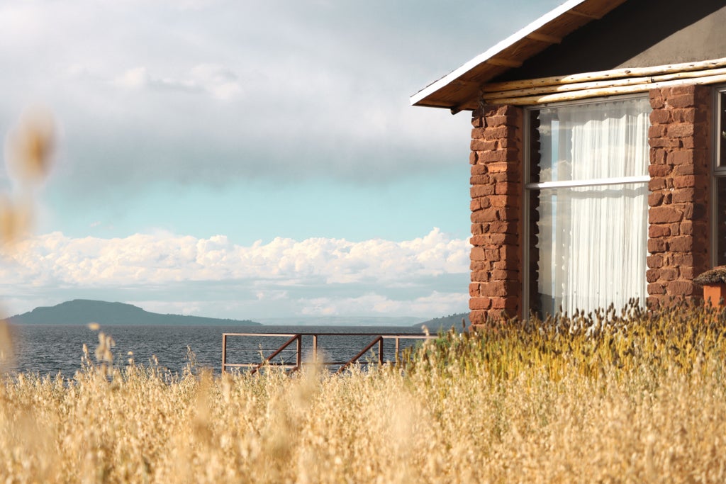 Luxurious stone lodge with floor-to-ceiling windows overlooking Lake Titicaca at sunset, featuring modern terrace and native landscaping