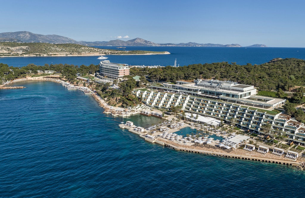 Elegant oceanfront resort with modern white buildings cascading down a hillside, surrounded by pine trees and Mediterranean waters