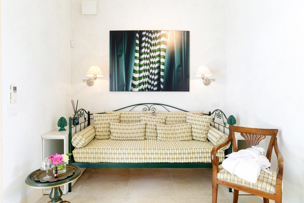 Elegant Sicilian boutique hotel room with soft white linens, rustic stone walls, traditional wooden furniture, and warm natural light filtering through linen curtains