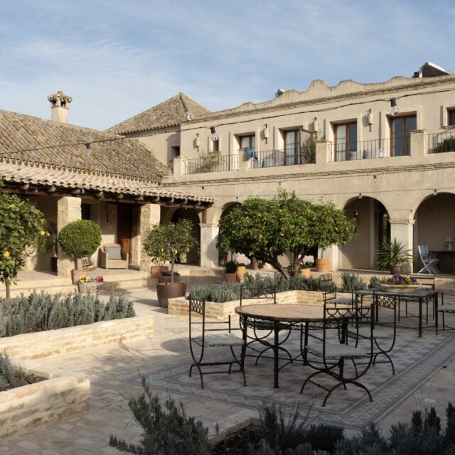 Elegant Spanish boutique hotel with whitewashed walls, terracotta roof, and leafy courtyard surrounded by rustic stone arches