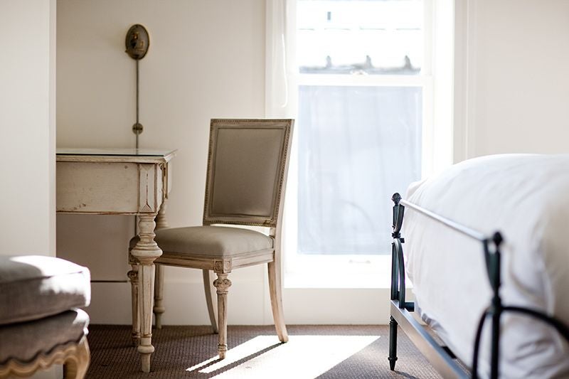 Elegant town king room with plush white bedding, refined wood furnishings, large windows, and soft neutral color palette in historic scenset hotel setting