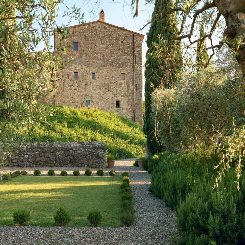 Rustic stone Tuscan villa with elegant infinity pool overlooking rolling vineyards and olive groves at golden sunset in rural Italian countryside