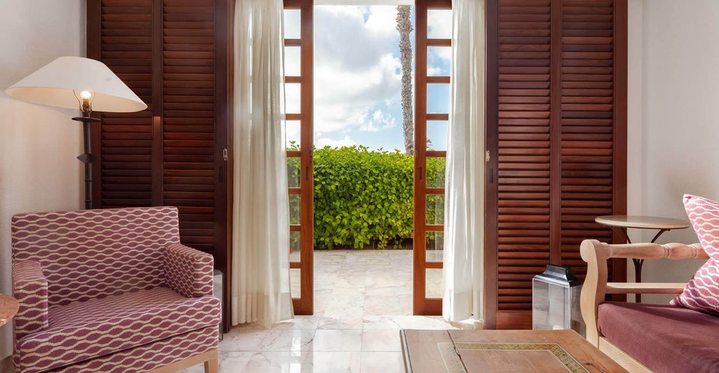 Spacious garden studio suite with modern decor, plush white bedding, elegant wooden floors, and sliding glass doors to a lush tropical terrace.