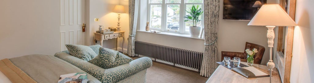 Luxurious forest-view hotel room with plush bedding, rich wooden furnishings, and large windows overlooking lush greenery at The Forest Side in the United Kingdom.