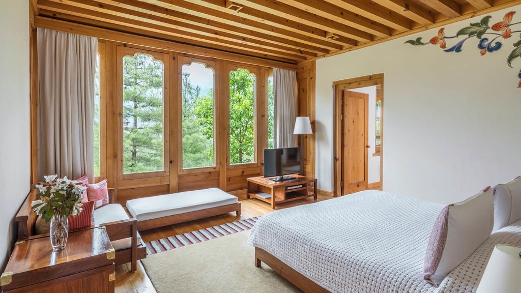 Spacious one-bedroom villa with traditional Bhutanese wood furnishings, floor-to-ceiling windows overlooking mountain landscape at luxury COMO Uma Paro resort