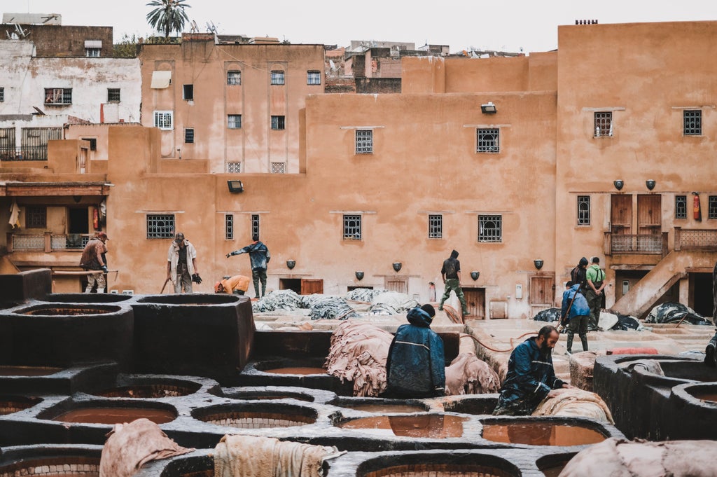 Sunlit alleyway in Marrakech's Medina, ornate mosaic tiles, traditional Moroccan architecture, vibrant textiles, and intricate archways casting elegant shadows