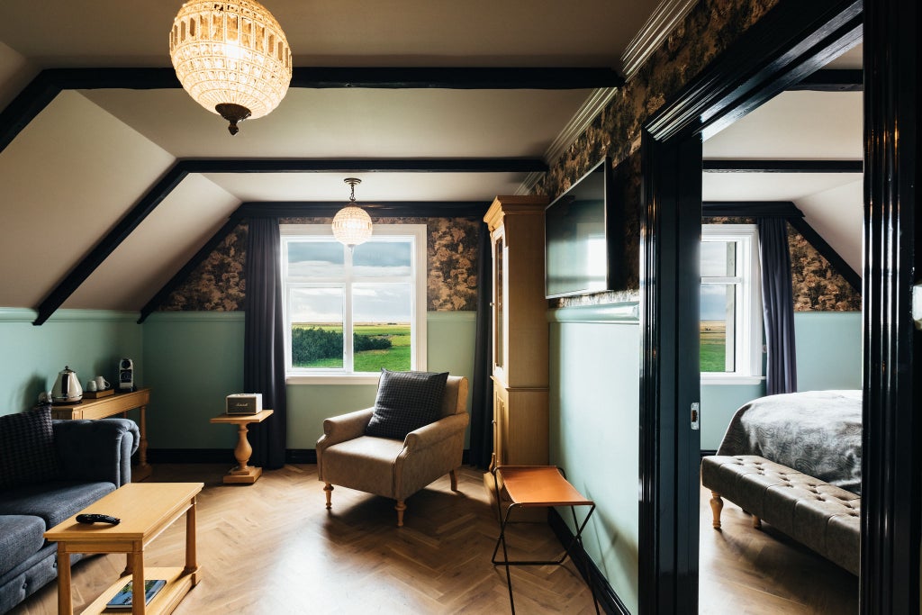 Rustic yet elegant Icelandic hotel with wooden facade, nestled against dramatic mountain backdrop and rolling green hills at sunset