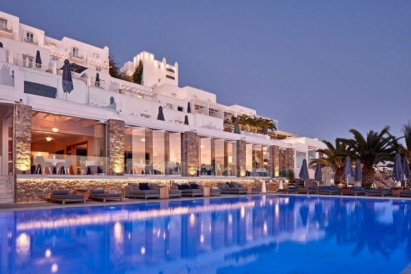 Luxurious whitewashed Scenset hotel overlooking the Aegean Sea, with elegant infinity pool, sun loungers, and stunning blue-domed architecture of Mykonos